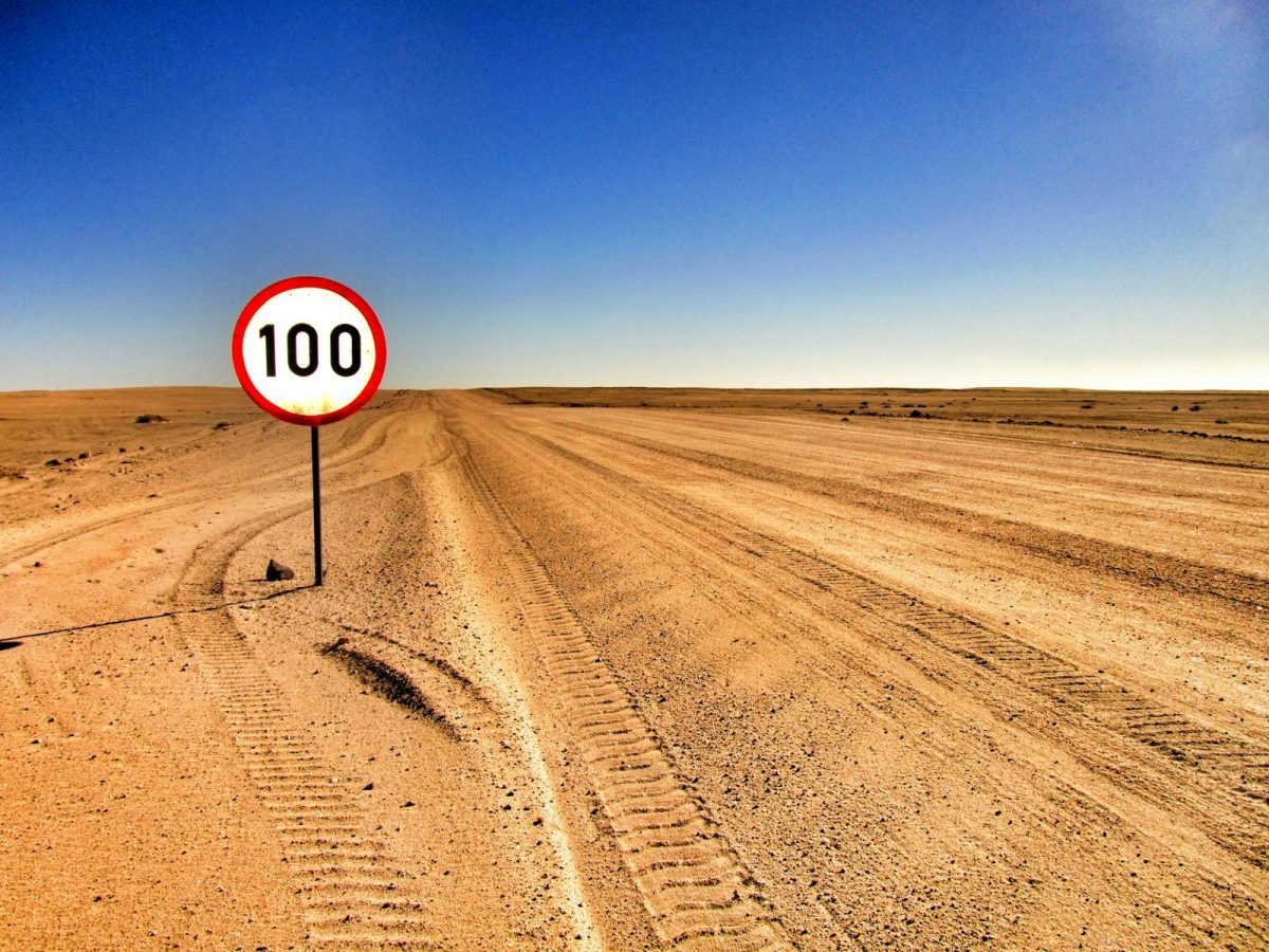 Open desert road with a speed limit sign showing 100 under clear sky.