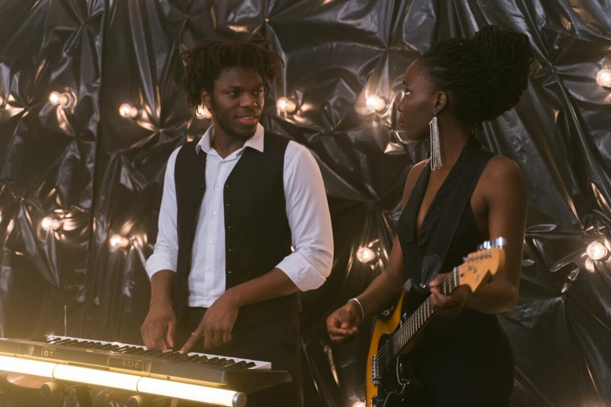 A male pianist and female guitarist perform together in a stylish indoor setting.