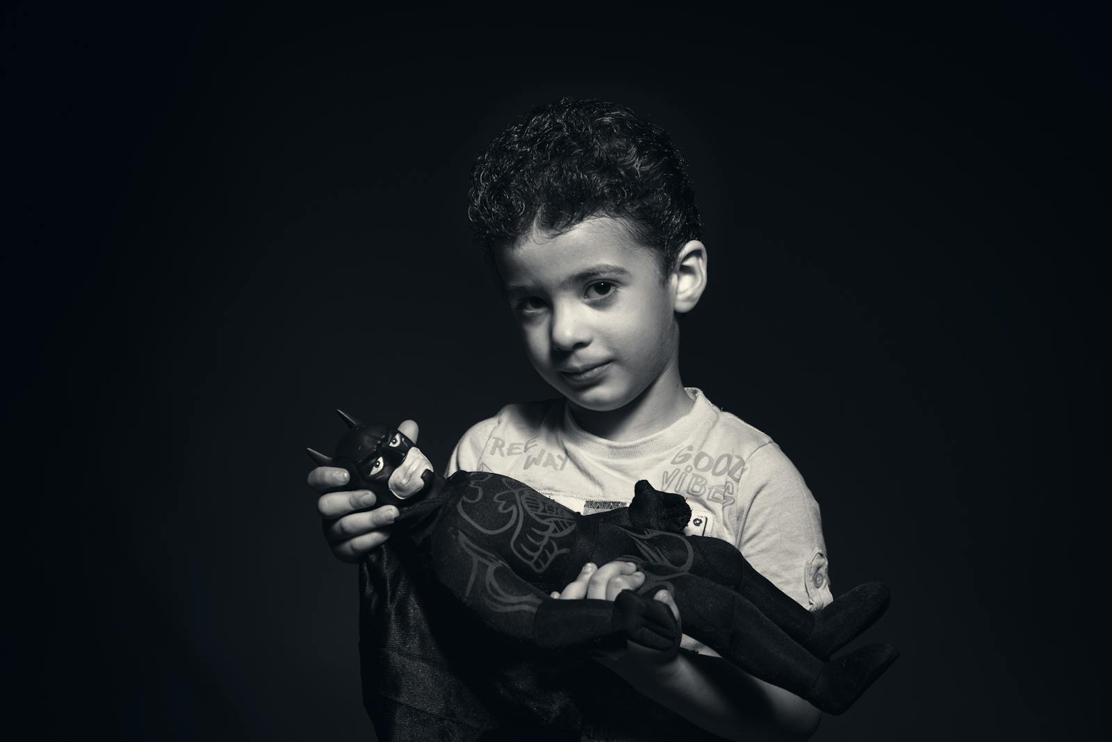 A young boy holding a Batman toy captured in a striking black and white portrait.