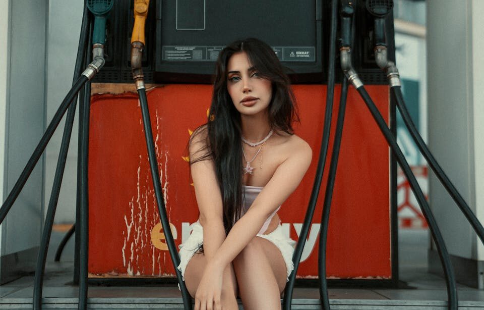 Stylish woman in sneakers sitting at a gas pump in a modern gas station setting.