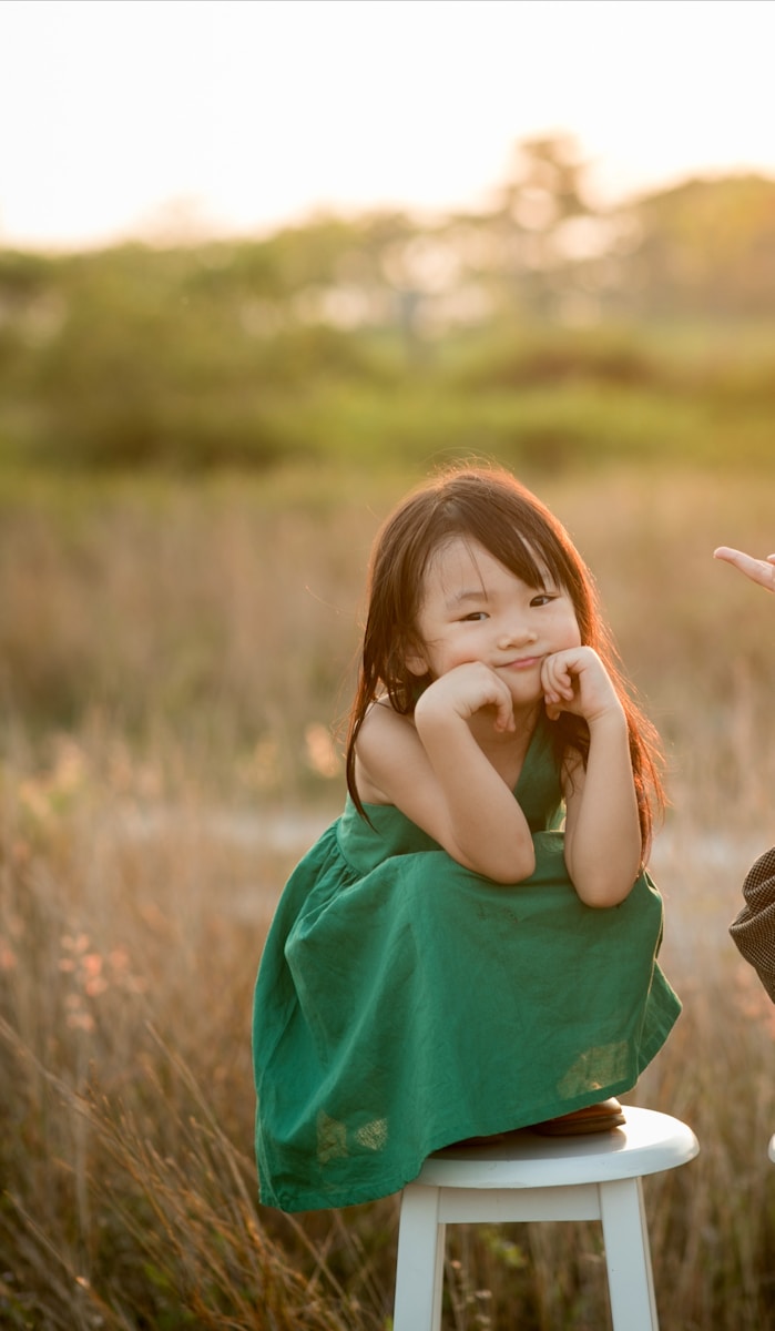a little girl sitting on a stool in a field