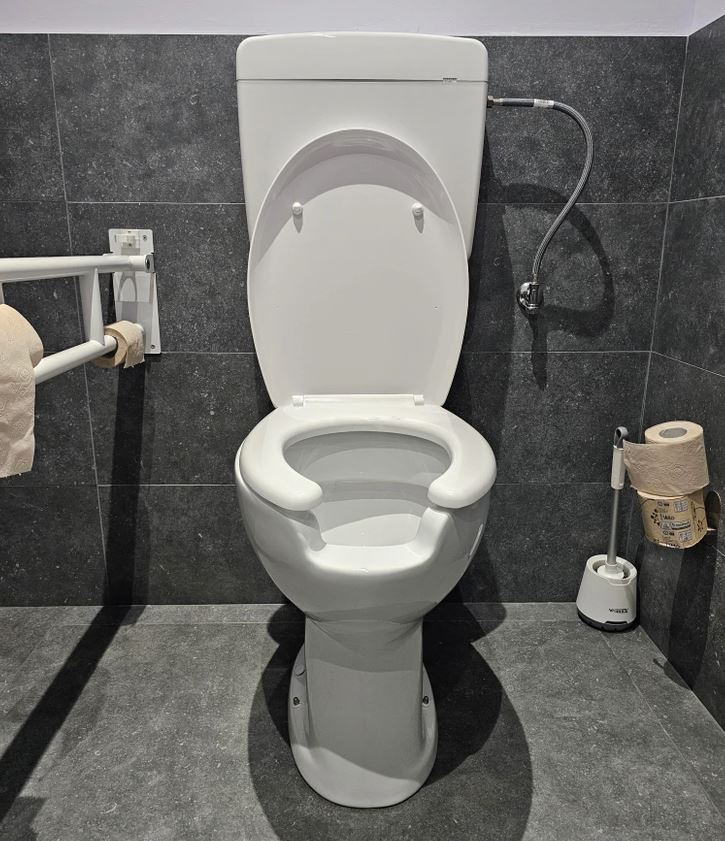 Toaleta s bidetom v modernej kúpeľni, vedľa úchytka s toaletným papierom a toaletná kefa na podlahe.