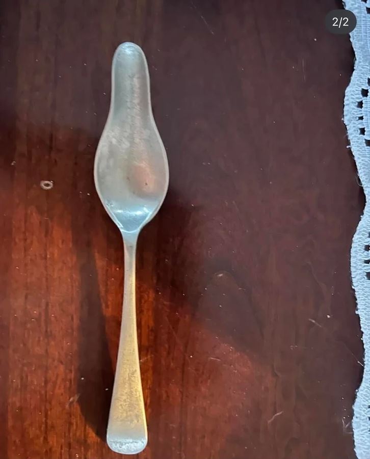 Starobylá strieborná lyžica položená na drevenom stole vedľa krajkového obrusu.