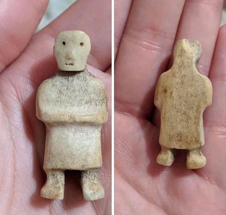 Malá soška z kostí vo forme postavy, zobrazená z prednej a zadnej strany na dlani.