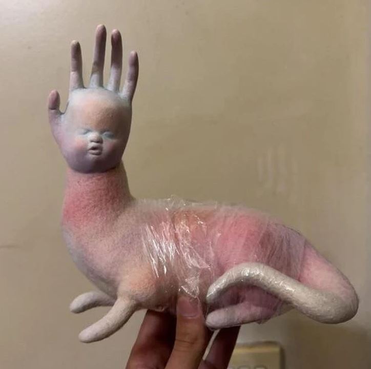 Neobvyklá socha: telo zvieraťa s ľudskou tvárou a rukou zdobená v pastelových farbách, podložené pastovým obalom.