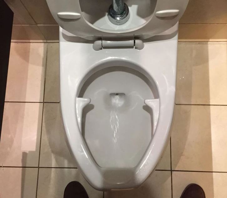 Moderná toaleta s prúdom vody, pohľad zhora. Čistý dizajn na svetlej dlažbe.