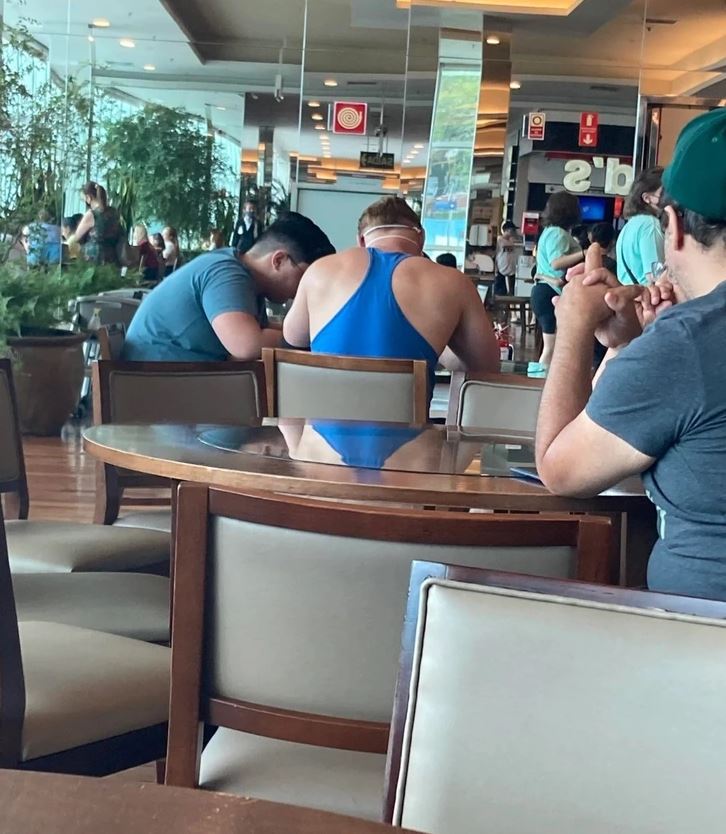 Dve osoby sediace pri stole v kaviarni, pohľad zozadu, príjemná atmosféra a zeleň v pozadí.