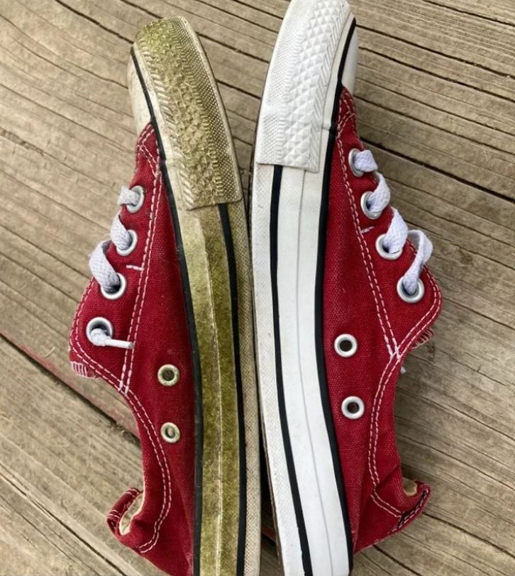 Dve červené tenisky na dreve: jedna opotrebovaná, druhá čistá. Výrazný kontrast stavu povrchu a podrážky.