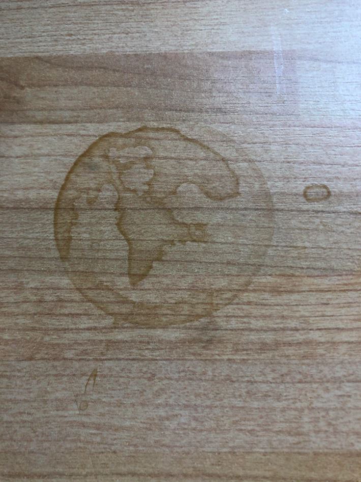 Odtlačok mokrého pohára zobrazujúci tvar sveta na drevenom povrchu.