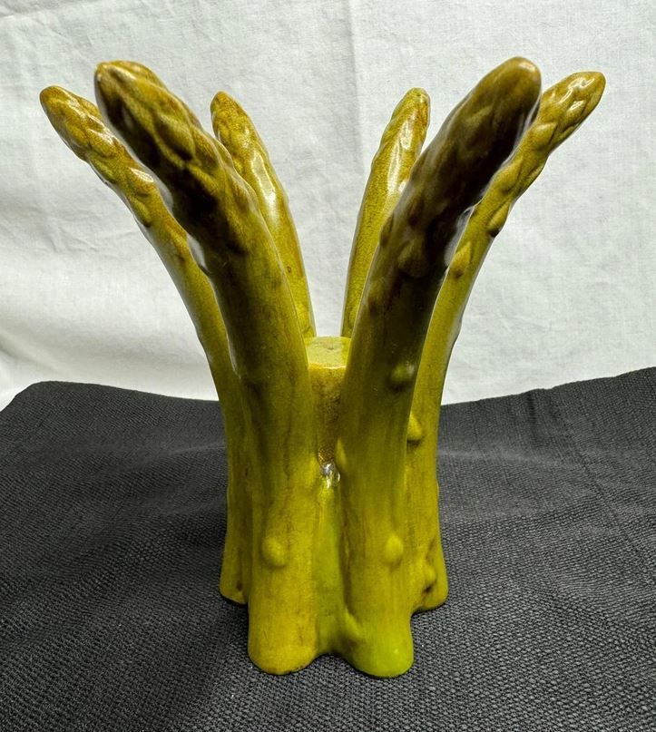 Keramická váza v tvare zväzku zelených šparglí na čiernom podklade.