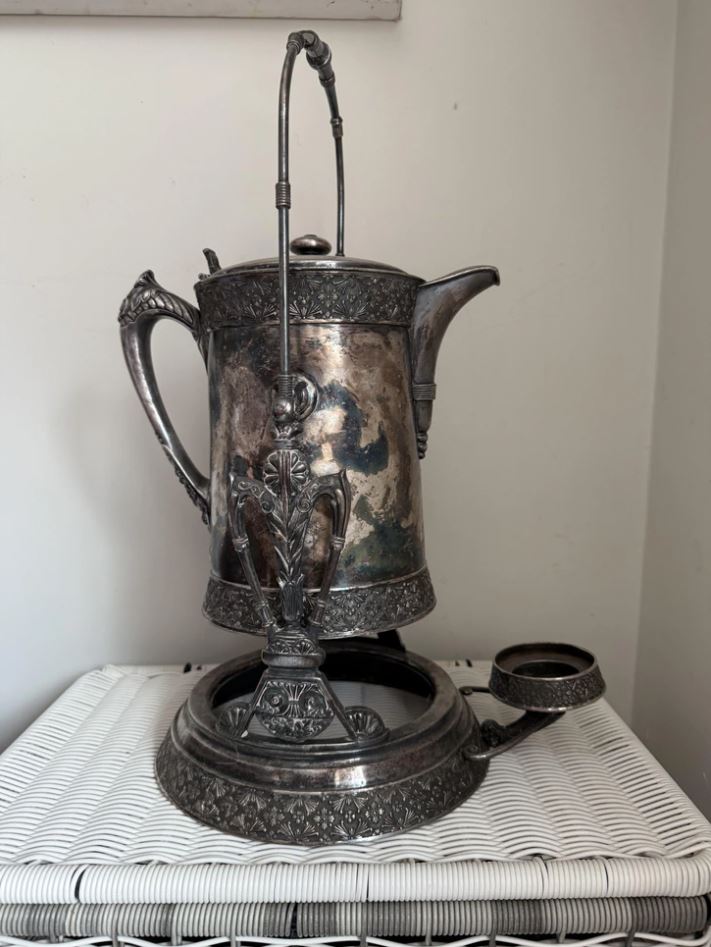 Starobylá kovová kanvica s dekoratívnymi detailmi na bielej podložke.