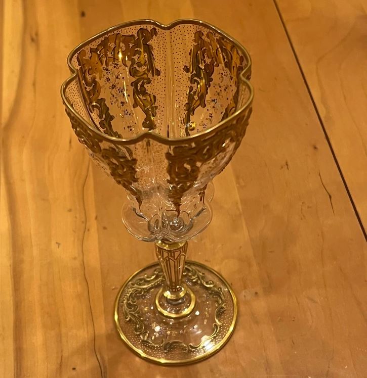 Ozdobný krištáľový pohár s vyrezávanými zlatými ornamentmi na drevenom stole.