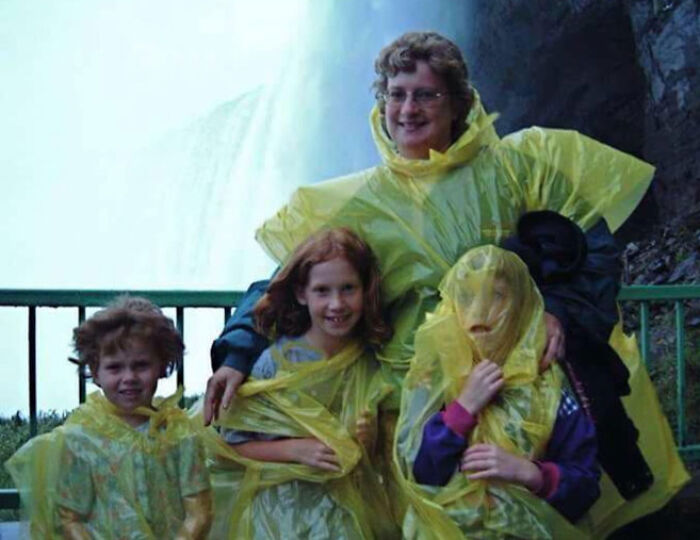 Rodina v žltých pláštenkách stojí pred vodopádom na vyhliadkovej plošine, usmieva sa a pózuje.