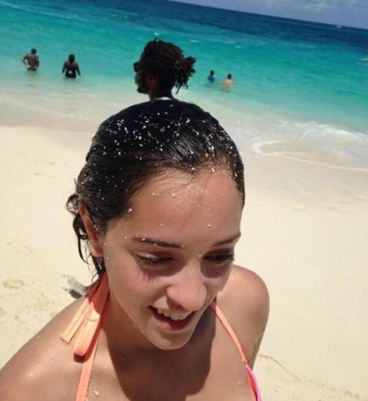 Opaľujúca sa žena na piesočnej pláži pri tyrkysovom mori, vzadu ľudia vo vode.