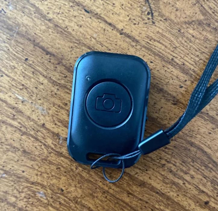 Bezdrôtová spúšť fotoaparátu na drevenom povrchu s pripevneným remienkom.