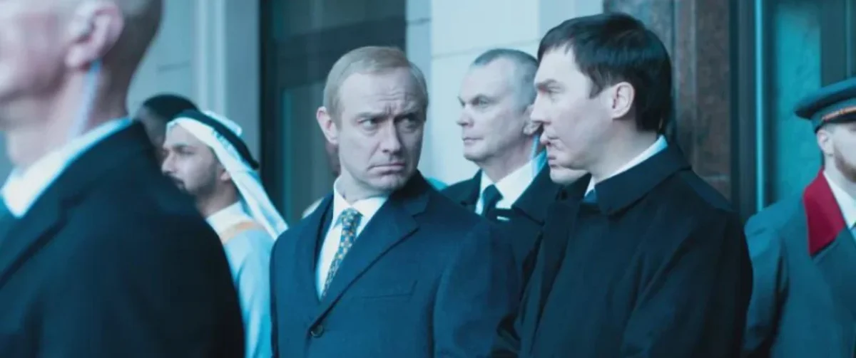 Muži v oblekoch diskutujú na verejnom podujatí, prítomný je aj muž v tradičnom arabskom oblečení.