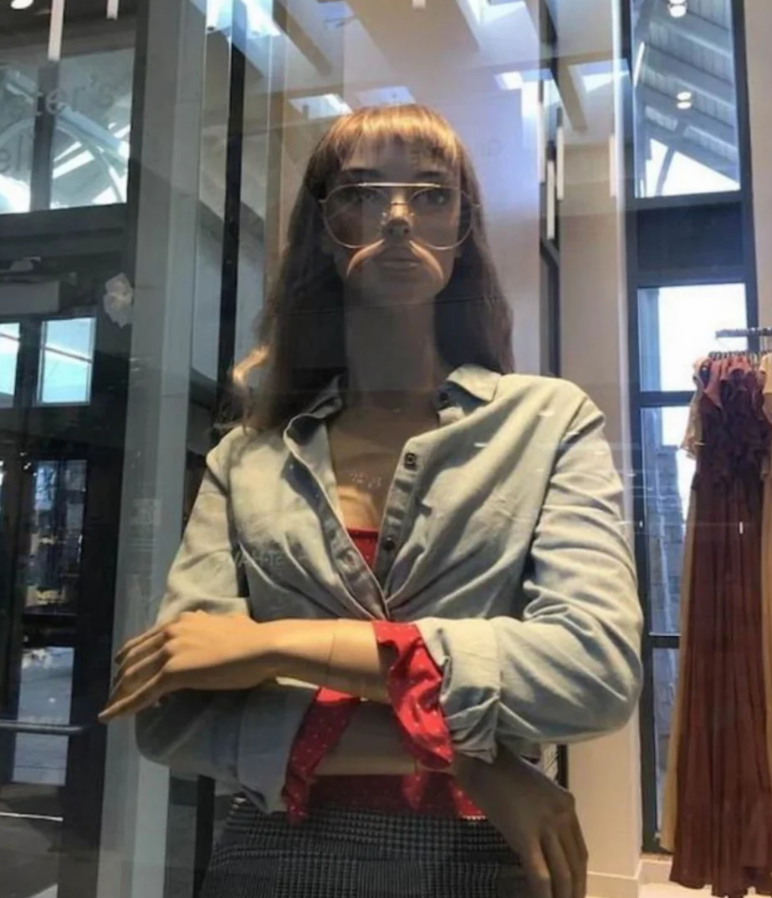 Manekýna v obchode s kockovanou sukňou a okuliarmi, odrážajúca sa vo výklade.