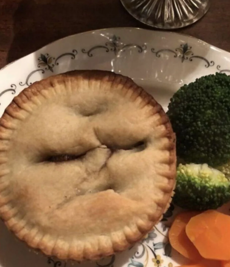 Koláč s výrazom tváre na dekoračnom tanieri, podávaný s brokolicou a mrkvou.