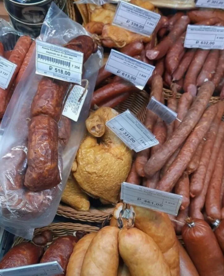 Rôzne druhy klobás a údenín s cenovkami v obchode, zobrazené na pultovom displeji.