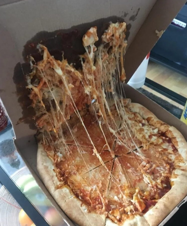 Rozliata pizza v krabici s roztopeným syrom, ktorý sa ťahá po vnútornom veku.