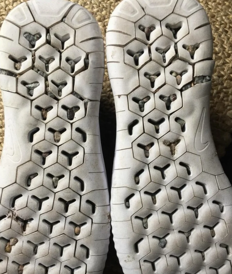 Pohľad na podrážky športových topánok s kamienkami zachytenými v šesťuholníkovom vzore.