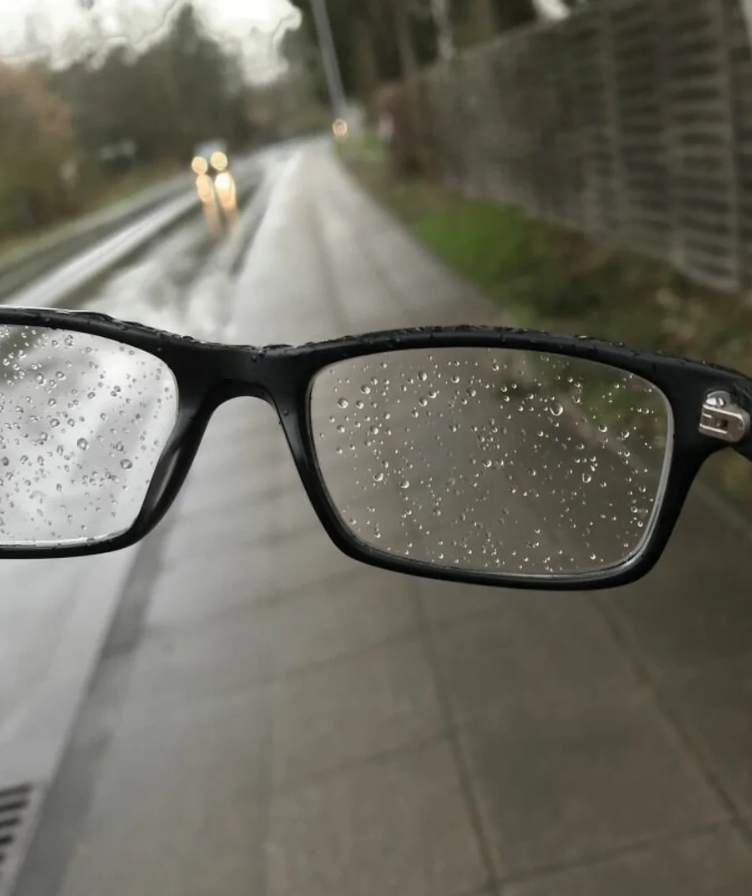 Okuliare s dažďovými kvapkami, rozmazaná cesta v pozadí.
