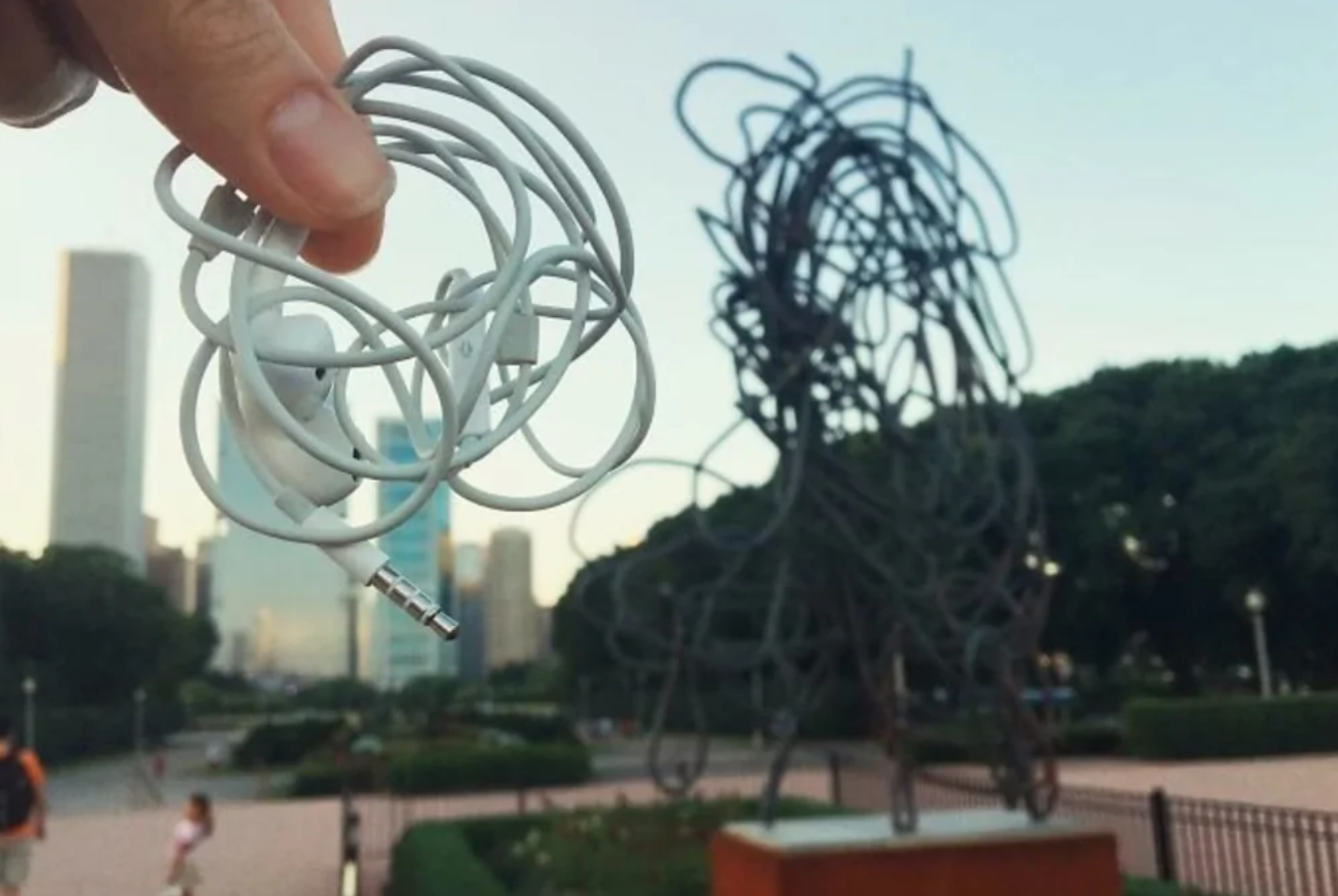 Zamotané slúchadlá pred sochou v parku za slnečného dňa, pripomínajúce moderné umenie.