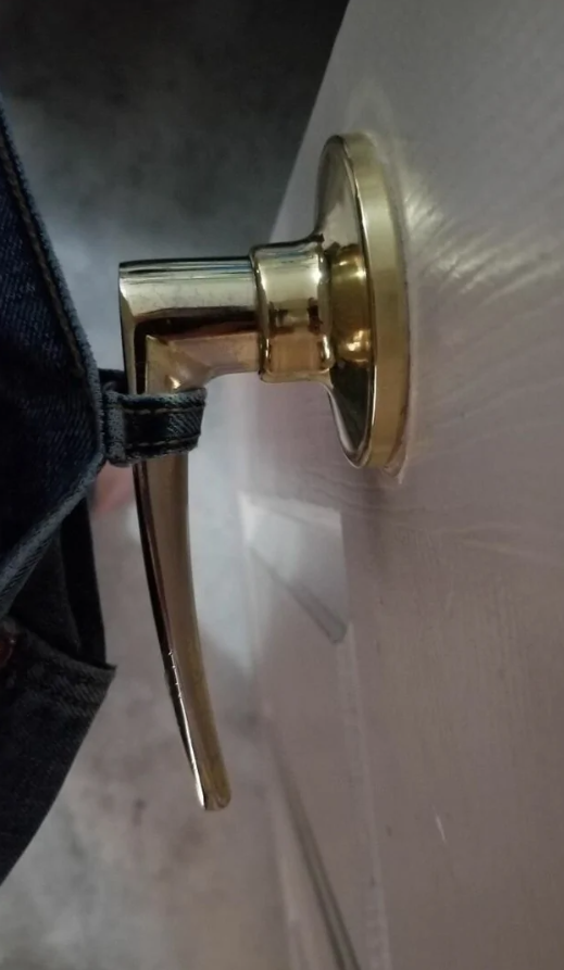 Dvere s mosadznou kľučkou zachytenou o džínsy, ukazujú nečakanú situáciu v domácnosti.