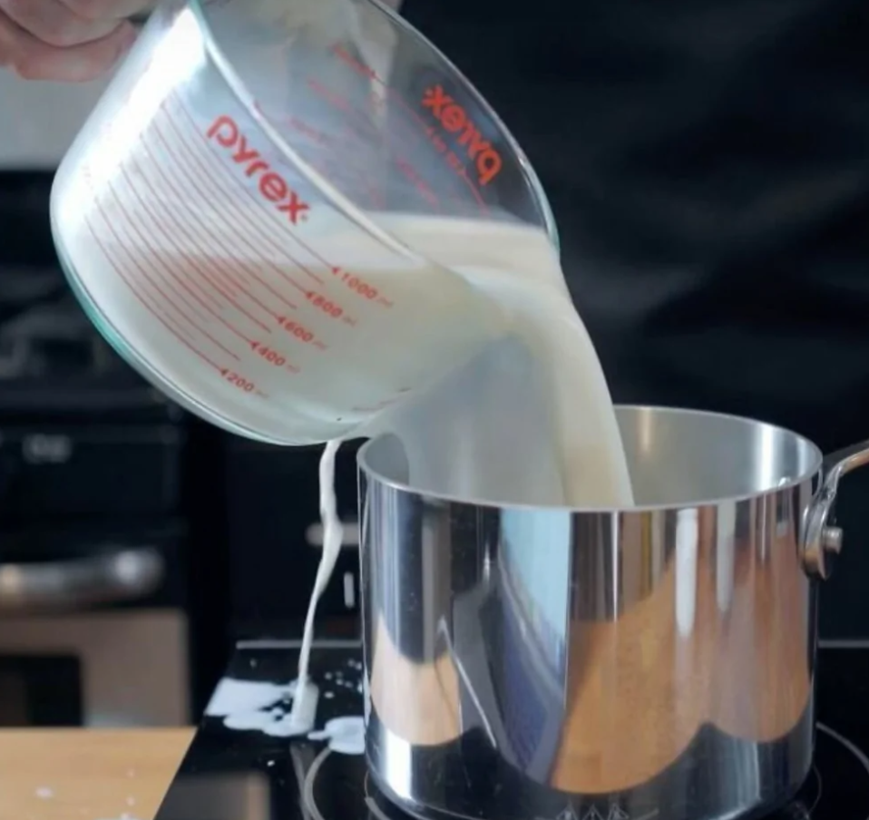 Mlieko sa leje z odmerky do hrnca na prípravu jedla v kuchyni.