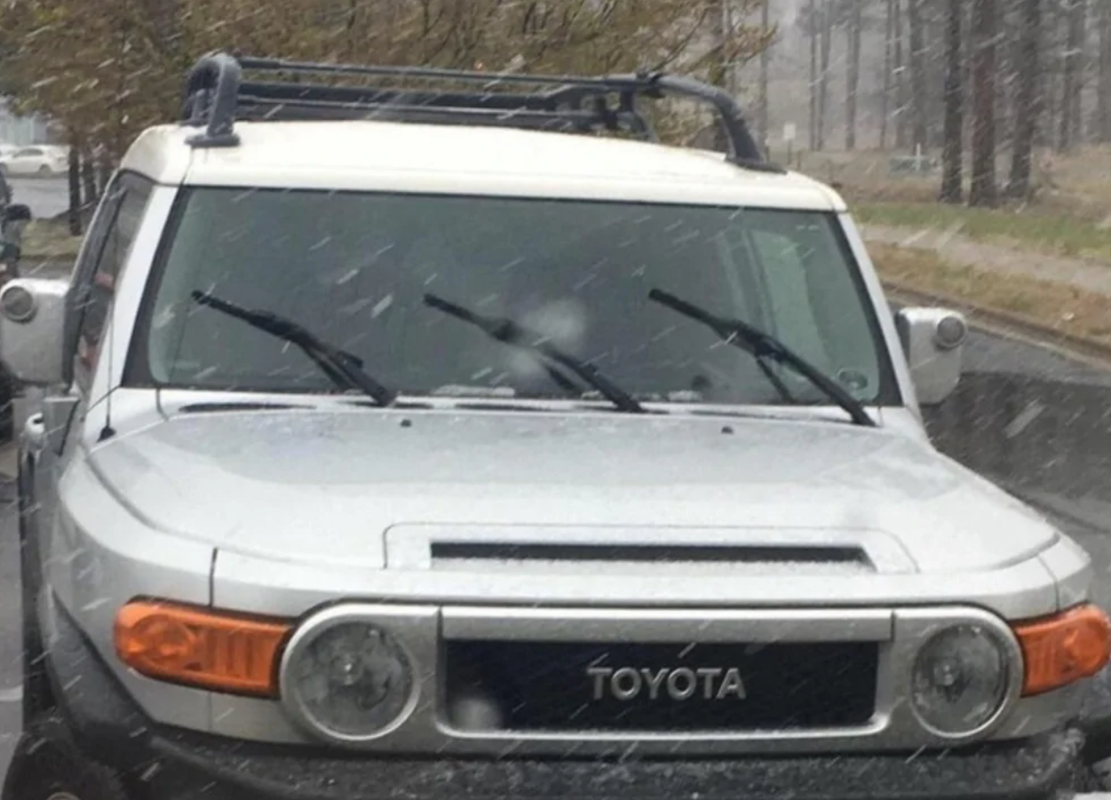 Toyota SUV stojí v daždi na ceste obklopenej stromami.