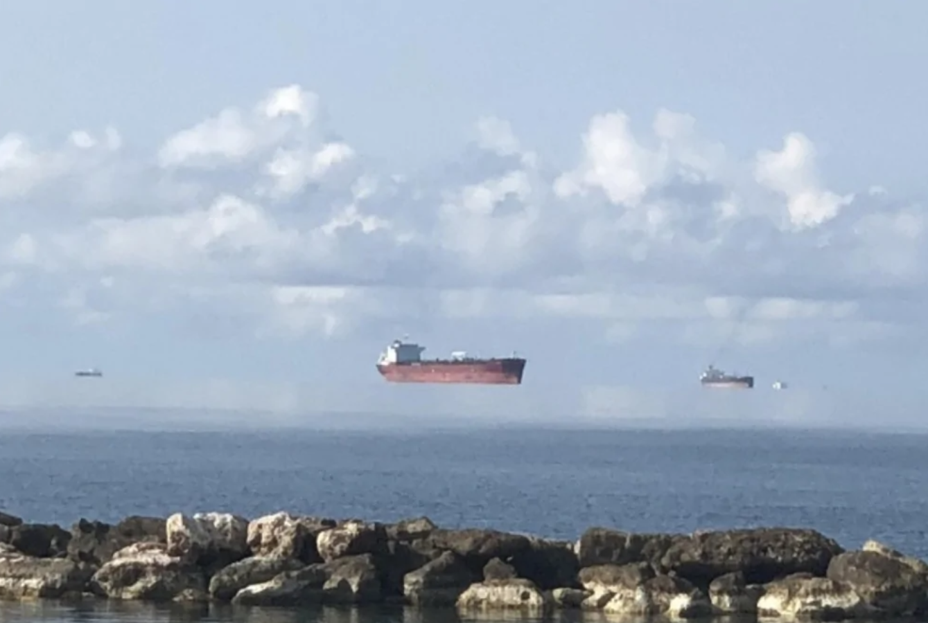 Ilúzia plávajúcej lode nad hladinou mora pri skalnatom pobreží a oblohe s oblakmi.