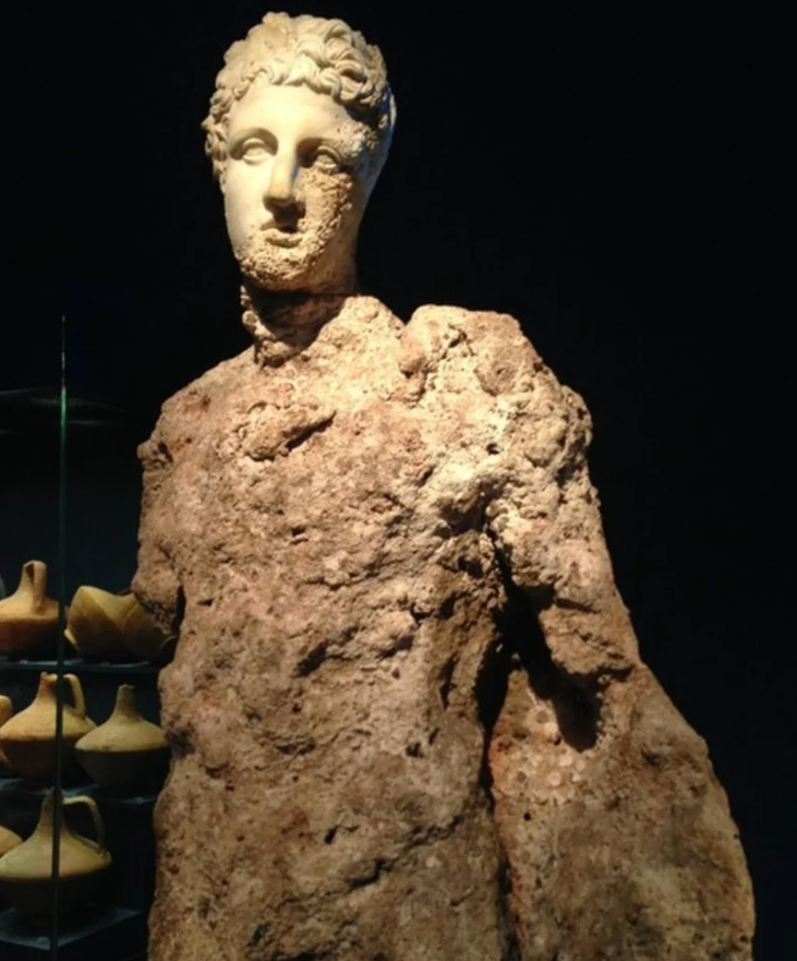 Antická socha bez rúk pokrytá koralmi vystavená v múzeu na tmavom pozadí. Morská erózia na starovekom diele.