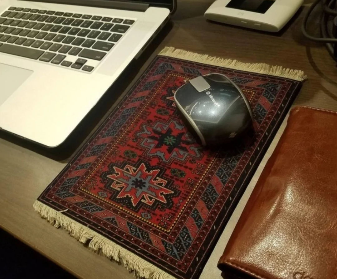 Používanie myši na podložke s orientálnym vzorom vedľa notebooku a koženého zápisníka.