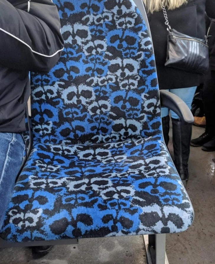 Sedlo v autobuse s modro-čiernym vzorom, obklopené stojacimi cestujúcimi v zimnom oblečení.