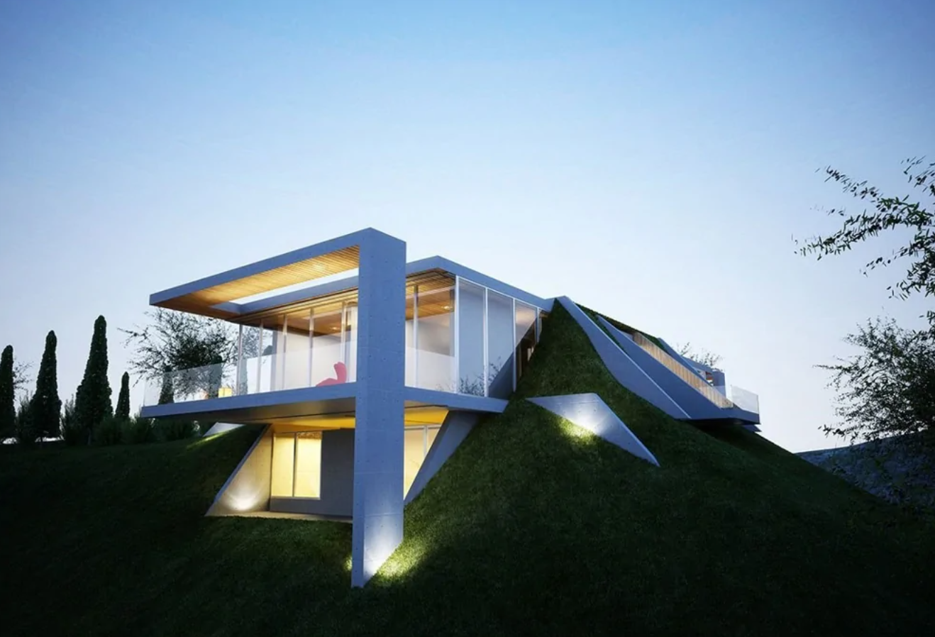 Moderný dom s presklenenými stenami, zakomponovaný do zeleného svahu pod modrou oblohou za súmraku.