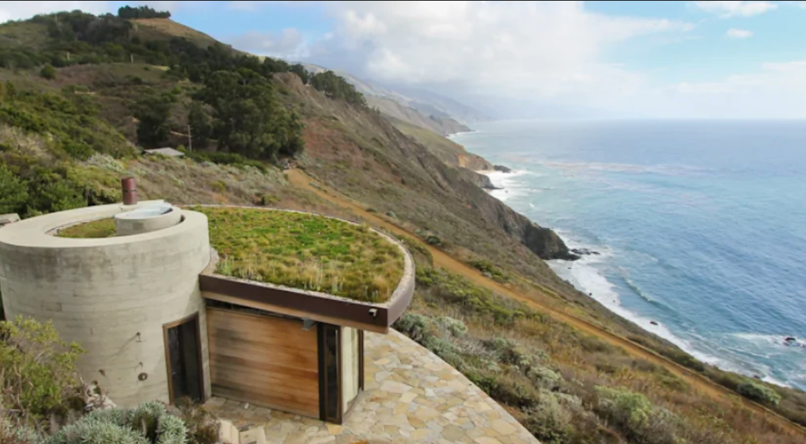 Moderný ekologický dom s trávnatou strechou na útesoch s výhľadom na oceán.