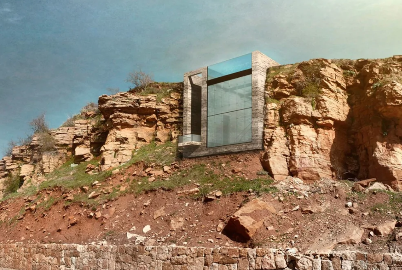 Moderná architektúra: Sklenený dom zabudovaný do skalnatého útesu pod modrou oblohou.