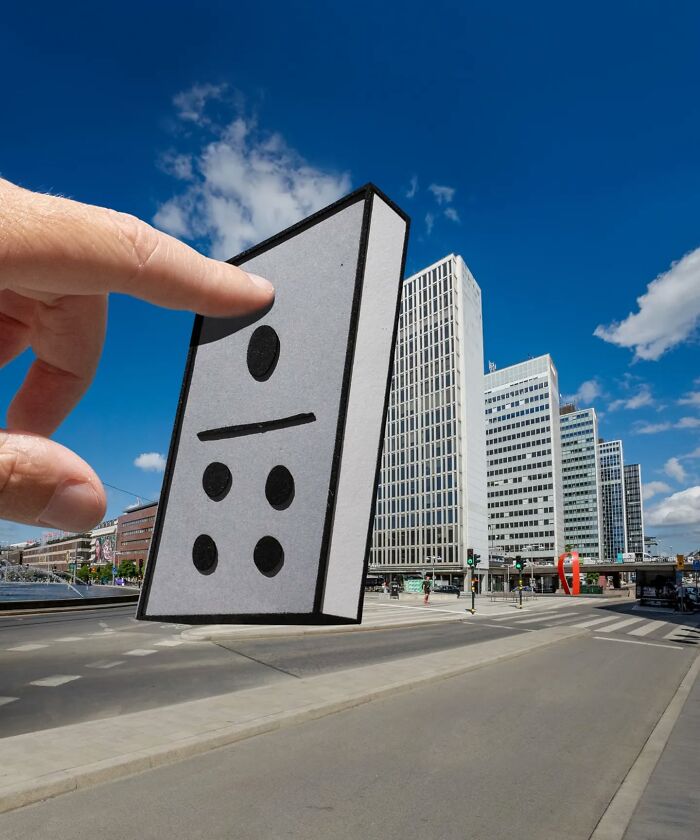 Ruka drží kartónový domino diel pri moderných výškových budovách pod modrou oblohou.