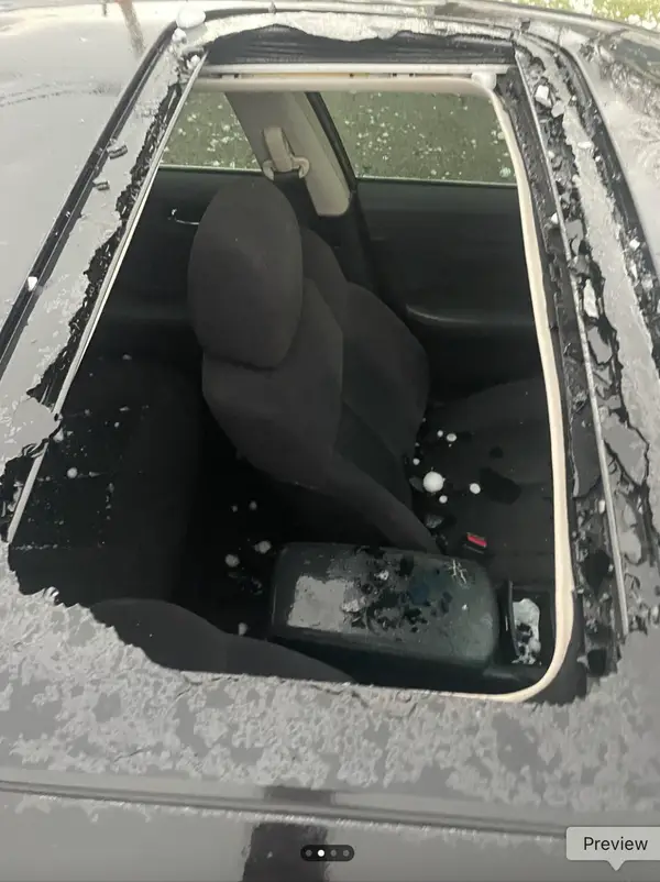 Strešné okno auta poškodené krupobitím, interiér pokrytý ľadovými guľkami.