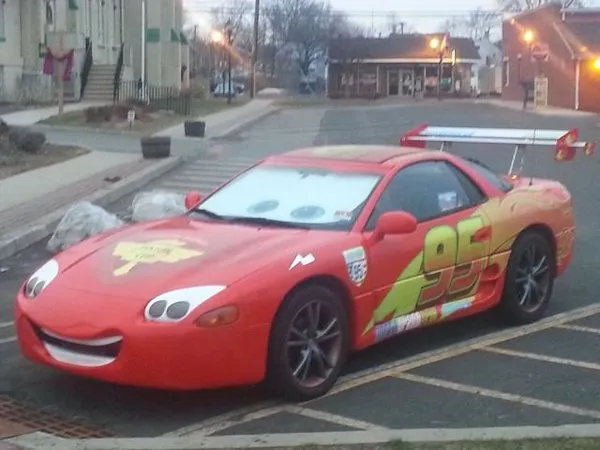 Červené auto upravené na motív postavy z animovaného filmu, zaparkované na ulici vedľa chodníka.