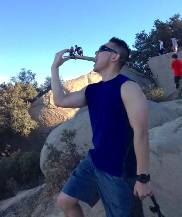 Muž v slnečných okuliaroch predstiera, že zjedá ľudí na horách v optickom klame.