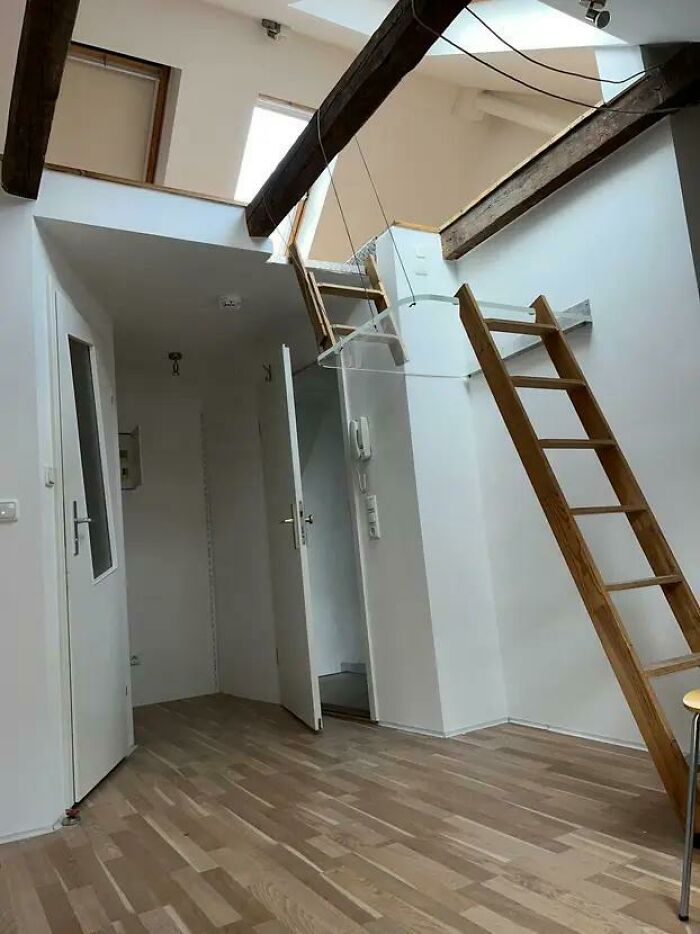 Podkrovná izba s dreveným schodiskom, svetlé steny a sklenené zábradlie, moderný dizajn interiéru.