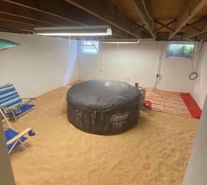 Vnútorná pláž s pieskom, nafukovacím bazénom a lehátkami, vytvorená vo suteréne s bielymi stenami.