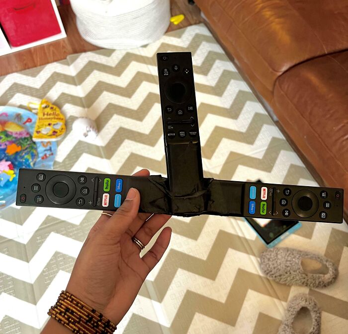 Trojuholníková konštrukcia z troch spojených diaľkových ovládačov držaná v ruke na farebnom koberci.