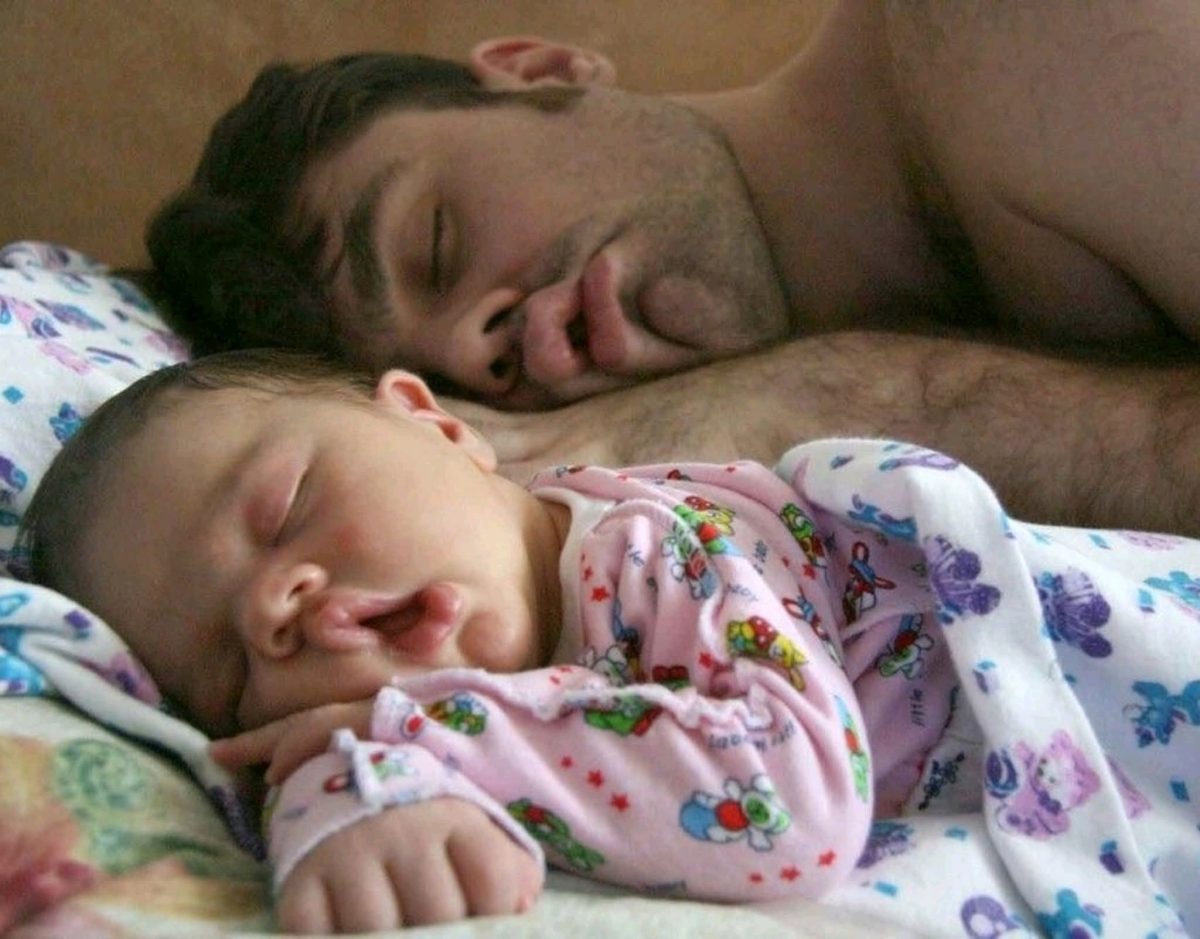 Otec a bábätko pokojnú spia vedľa seba pod farebnými dekami.