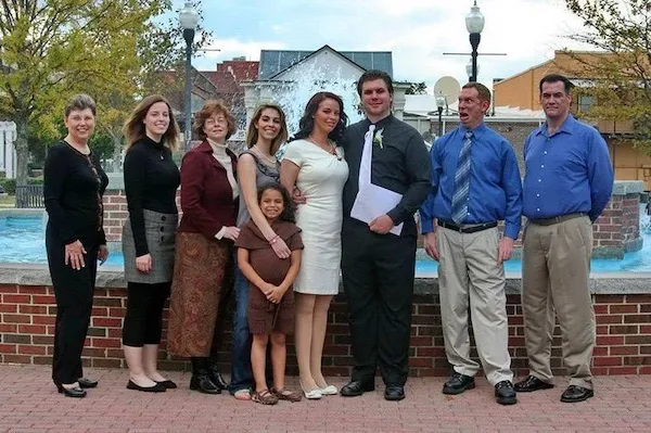 Skupina ľudí stojí pred fontánou na vonkajšom mieste, oblečení formálne aj neformálne.