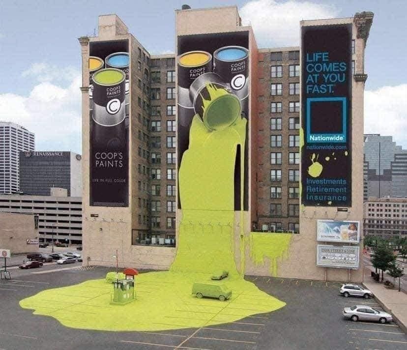 Obrovská plechovka zelenej farby preteká z plagátu na budove do parkoviska plného áut. Kreatívna reklama.