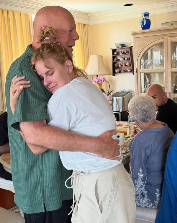 Ospravedlňujem sa, ale neviem určiť, kto sú ľudia na obrázku.Alternatívny text: „Ľudia sa objímajú v útulnej miestnosti pri stole s kvetmi.“