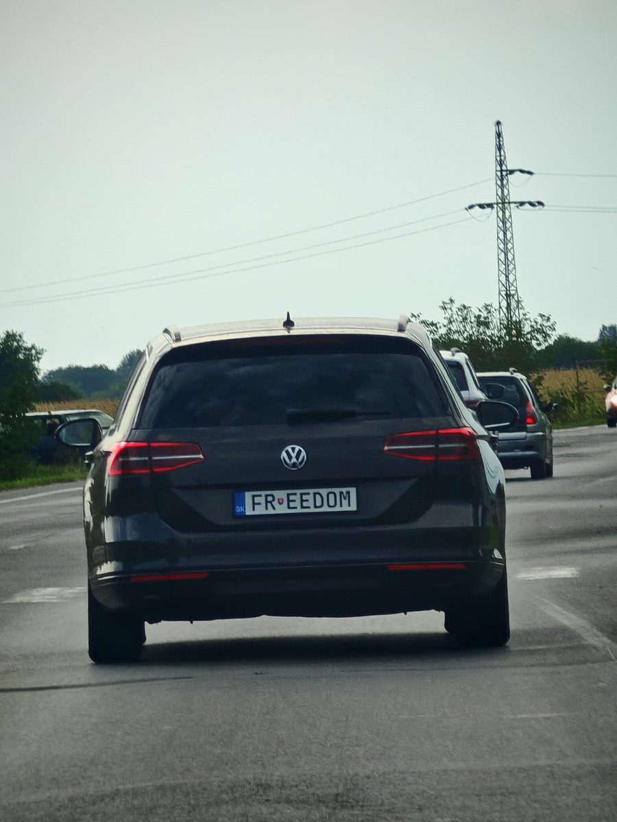 Neznáma ŠPZ s nápisom FREEDOM na čiernom Volkswagene idúcom po vidieckej ceste s ďalšími autami.