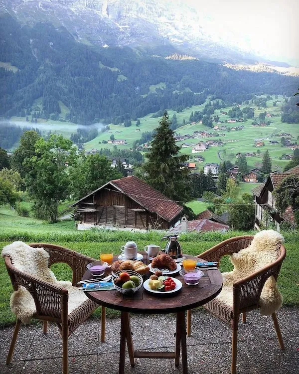 Raňajky s výhľadom na malebnú horskú dedinu so zelenými lúkami a drevenými chalúpkami v pozadí.